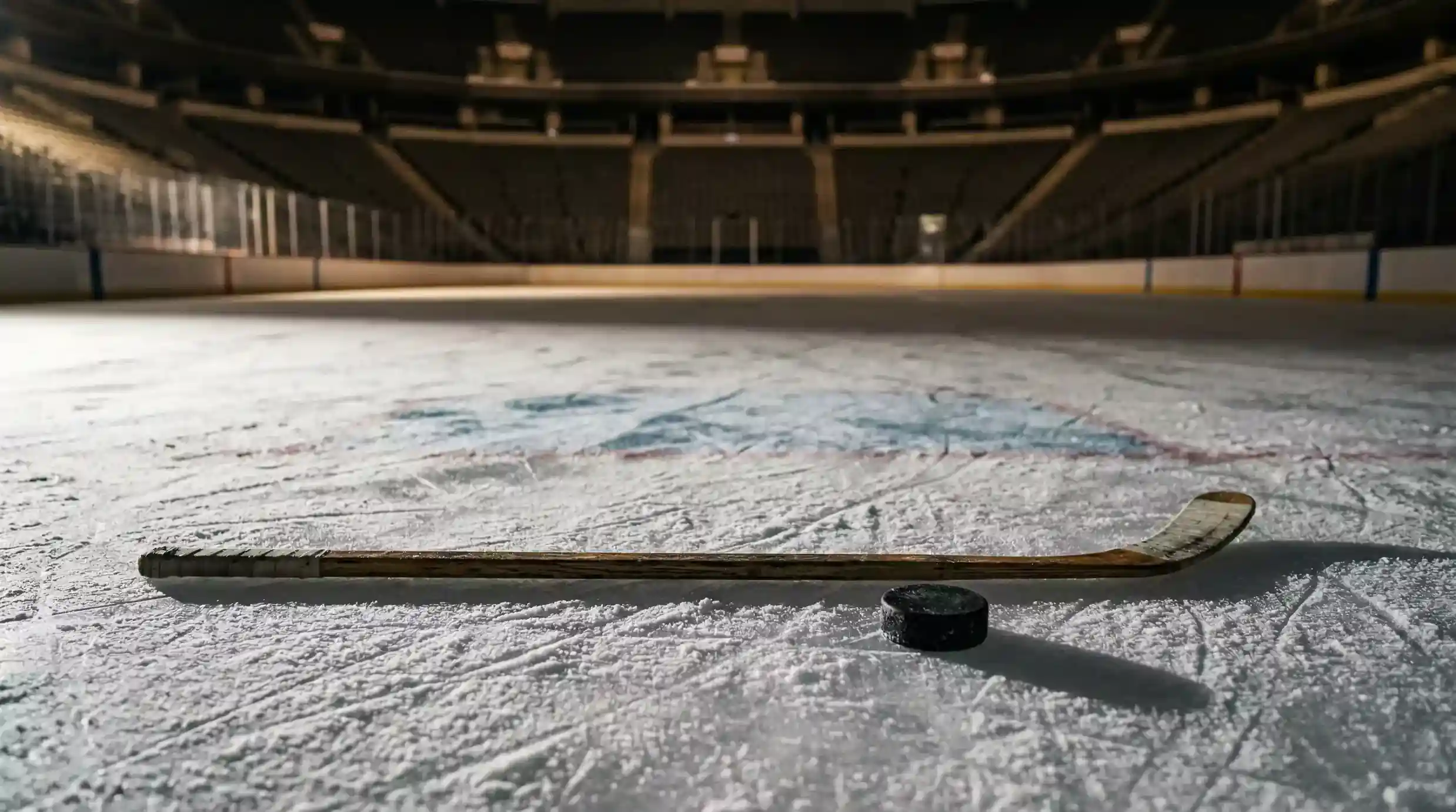 Ishockeyklubba som ligger på isen bredvid en puck i en tom arena